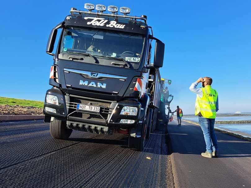 Bauleiter Kilian Efen im Gespräch mit seinem Fahrer. Das Bild zeigt die starke Neigung des Asphaltdeckwerks am Deich. | Foto: DAV/Quillmann Bauleiter Kilian Efen im Gespräch mit seinem Fahrer. Das Bild zeigt die starke Neigung des Asphaltdeckwerks am Deich. | Foto: DAV/Quillmann