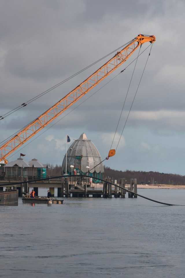Vom Kran des Arbeitsschiffs wird der knapp 400 m lange neue Rohrstrang auf dem Wasser schwimmend vorgehalten.