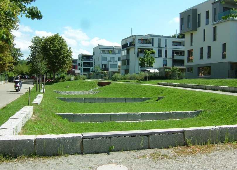 Freiburg im Breisgau, Wohnquartier „Östlich Wiehrebahnhof": Im abschüssigen Gelände liegen leicht vertieft Sickerbeete als ebene Grasflächen, kaskadenartig miteinander verbunden. Die Zuläufe sind als offene Rinnen ausgeführt. | Foto: König