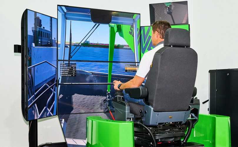 An Sennebogens Loghandling-Simulator steuert ein Besucher den virtuellen Holzumschlag über mehrere Bildschirme. | Foto: Sennebogen An Sennebogens Loghandling-Simulator steuert ein Besucher den virtuellen Holzumschlag über mehrere Bildschirme. | Foto: Sennebogen