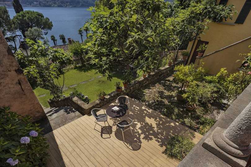 Der Blick von den Rundbogenarkaden im Obergeschoss auf den neugestalteten Außenraum unterstreicht, wie sehr sich „Die Naturlinie“ in den Garten einfügt und gleichzeitig zur traditionellen Architektur vor Ort passt – als wären die Dielen aus WPC von Naturinform schon immer dort gelegen. | Foto: www.keller-fotografie.de