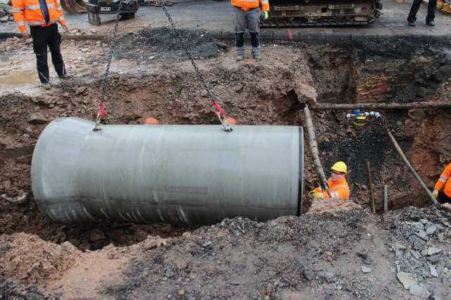 Die Rohre werden an einem Kettengehänge und in dem Rohr integrierten Kugelkopfankern mit dem Bagger in den Graben versetzt. | Foto: Ralph Mitterbauer