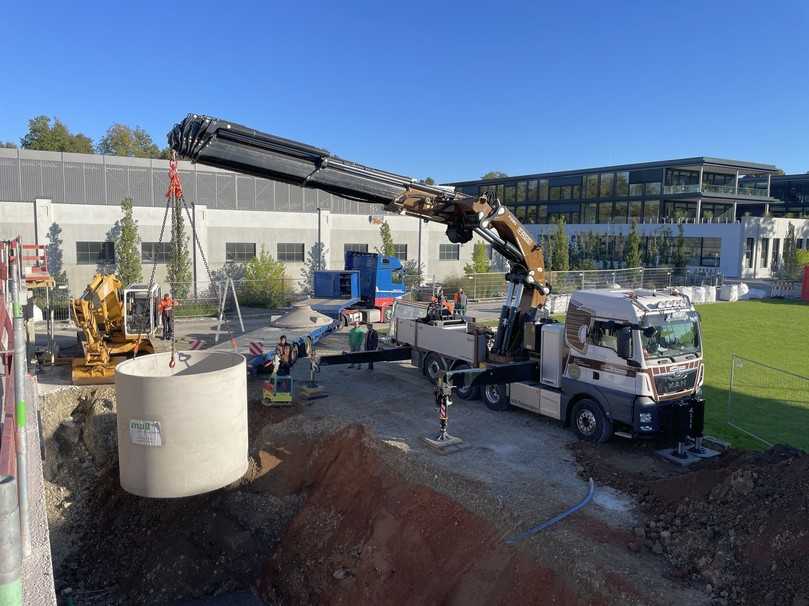 Versetzen der Regenspeicher vom Kran des Lieferfahrzeugs in die vorbereitete Baugrube vor der Südfassade: Fünf Betonbehälter, die untereinander verbunden sind, bilden die sogenannte Mehrbehälteranlage, der ein Filterschacht vorgeschaltet wurde. Dieser reinigt das vom Dach kommende Regenwasser. | Foto: Carderie KG