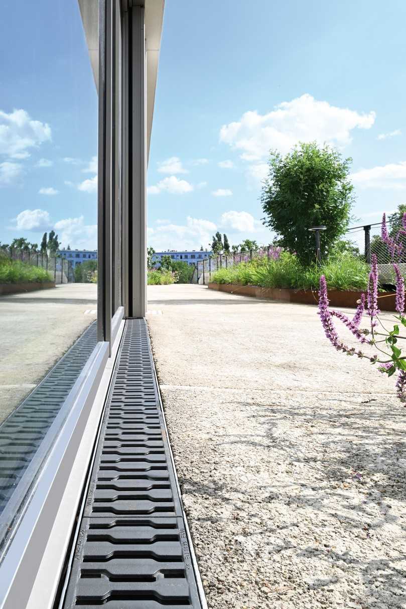 In den Laibungsbereichen an den Türen und Fenstern der Glasfassade stellen die Betonrinnen „Fortis“ zusammen mit den gusseisernen Designrosten „Zippa“ die Entwässerung sicher. | Foto: Richard Brink