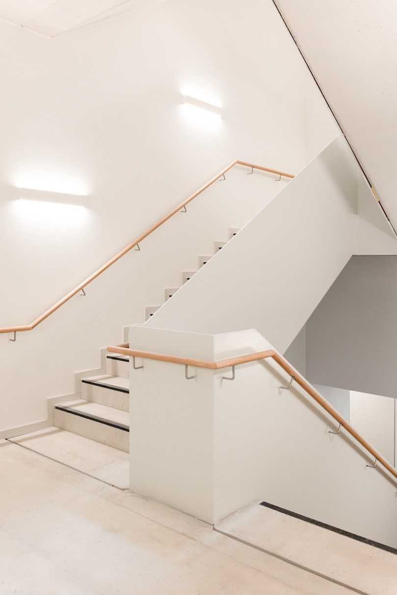 Das Fluchttreppenhaus nach Fertigstellung: Das  Zusammenspiel aus klassisch grauem Sichtbeton, Holzhandläufen sowie filigranen weißen Brüstungsblechen im Treppenauge sorgt für eine hochwertige Anmutung. | Foto: Schöck Bauteile GmbH / Arne Mayntz