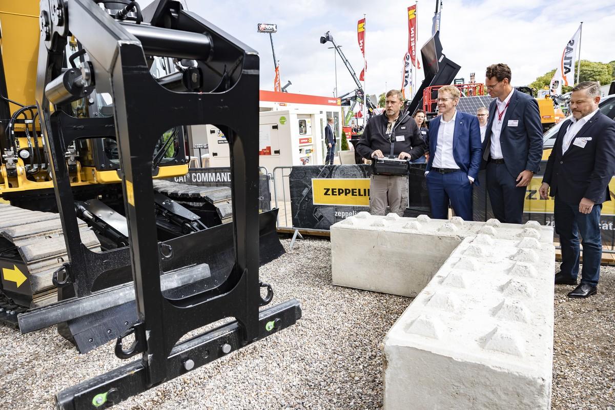 700 Ausstellerinnen und Aussteller präsentieren sich auf der Nordbau 2026 in Neumünster unter anderem auf dem Freigelände. Ministerpräsident Daniel Günther (2. v. li.) lässt sich die technischen Details von den Experten erklären. | Foto: Holstenhallen Neumünster – NordBau – SixConcept